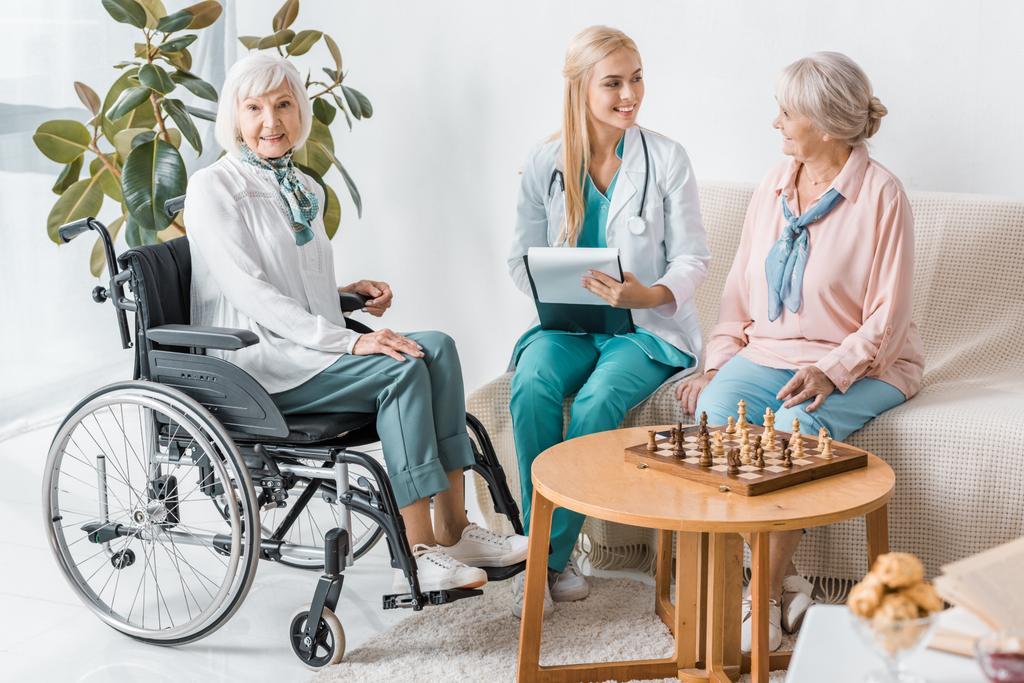 giovane infermiera sorridente seduta sul divano e che scrive prescrizione alle donne anziane
 - Foto, immagini