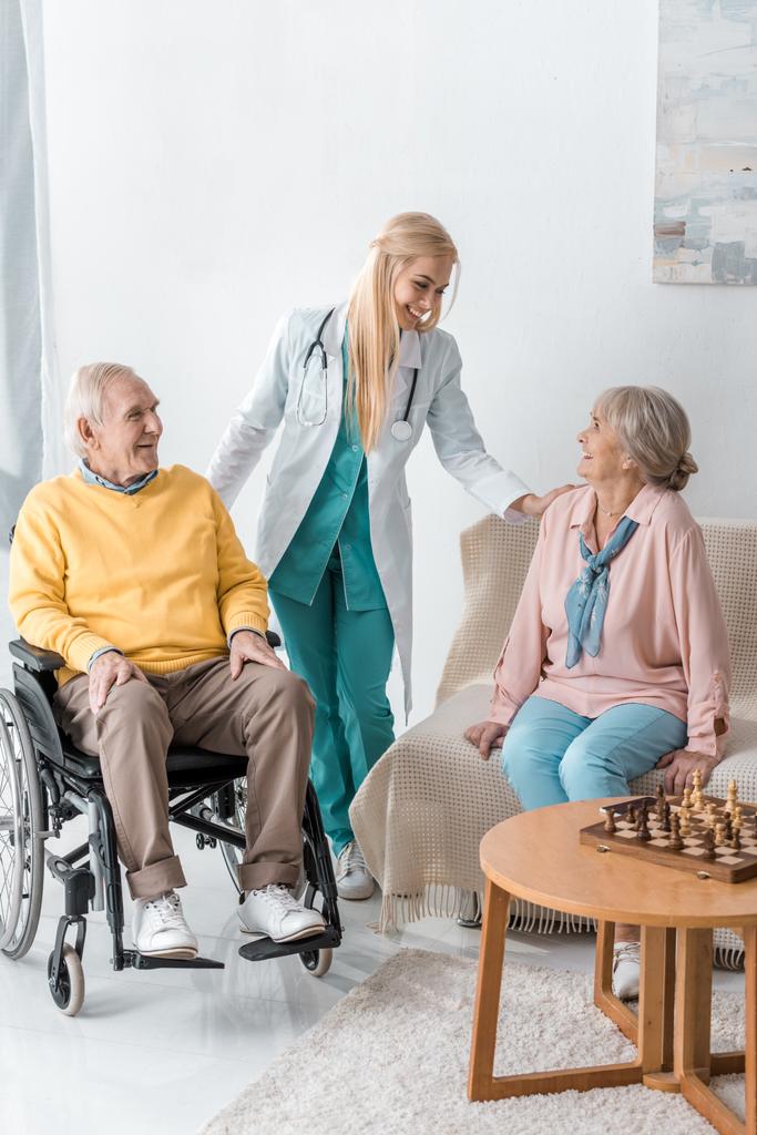 jovem médico feminino alegre conversando com pessoas idosas em casa de repouso
 - Foto, Imagem