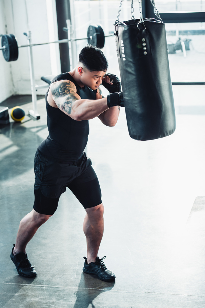 若いスポーツマン ボクシング手袋を着用し、パンチのジムでボクシング バッグ - 写真・画像