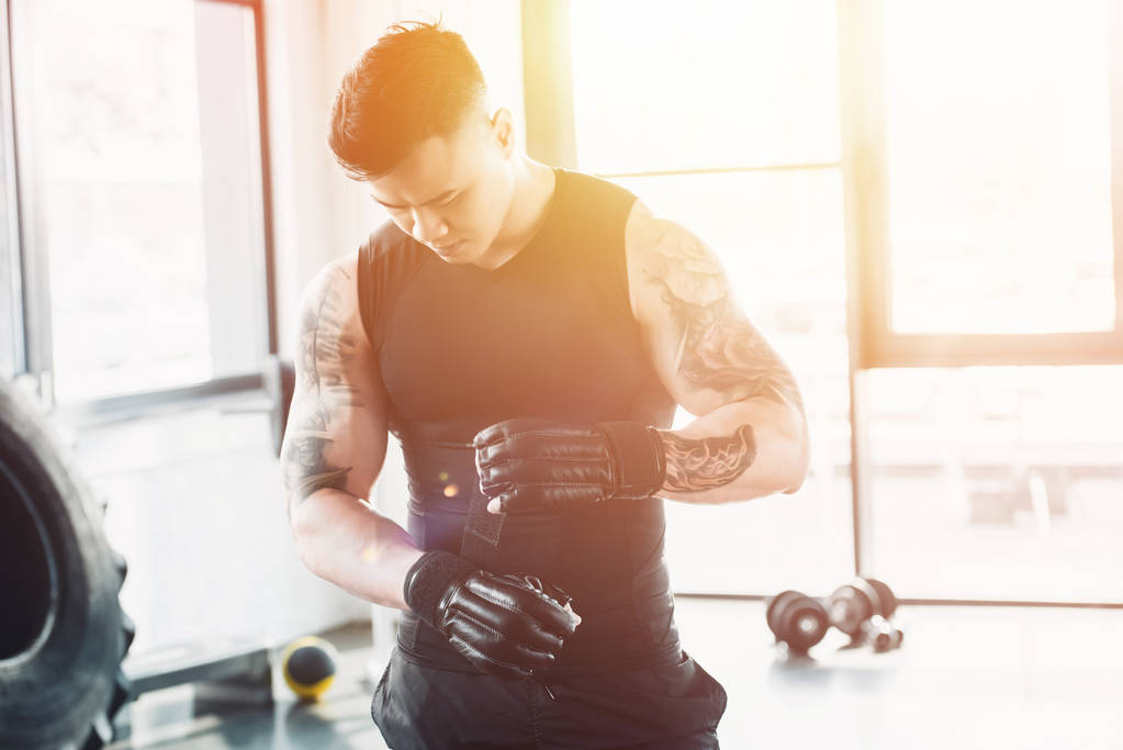 young asain sportsman wearing black boxing gloves at gym in sunlight - Photo, Image