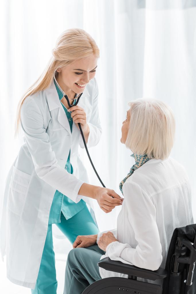 smiling female doctor examining with stethoscope disabled senior woman  - Photo, Image