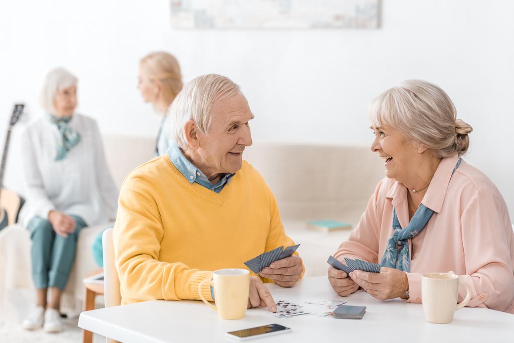 Glücklich lächelndes Seniorenpaar beim Kartenspielen am Tisch im Pflegeheim - Foto, Bild