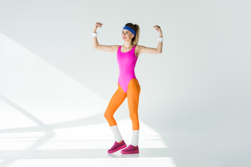 красивая улыбающаяся атлетическая девушка, показывающая бицепсы и глядящая в сторону серого
 - Фото, изображение