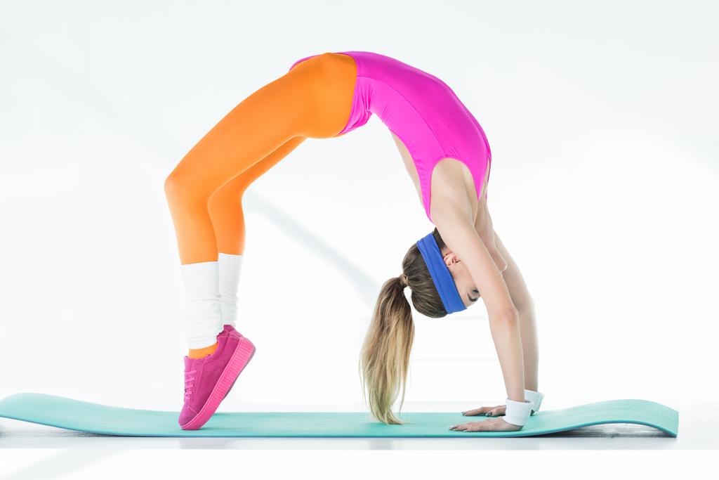 vista lateral de la joven atlética haciendo ejercicio de puente sobre estera de yoga en gris
 - Foto, imagen