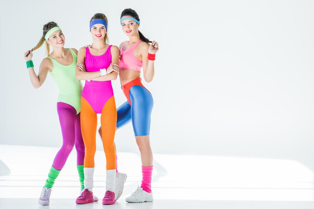 повнометражний вид красивих спортивних дівчат у стилі 80-х років спортивний одяг, посміхаючись на камеру на сірому
 - Фото, зображення
