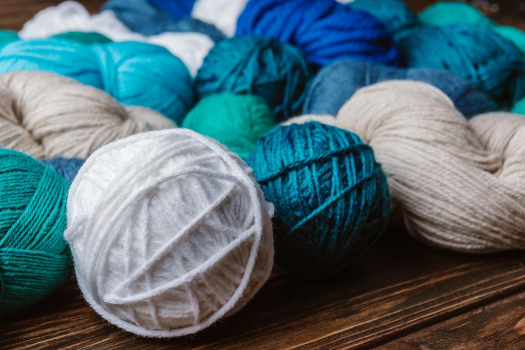 vista ravvicinata di filati bianchi, blu e verdi per la lavorazione a maglia su superfici in legno
 - Foto, immagini