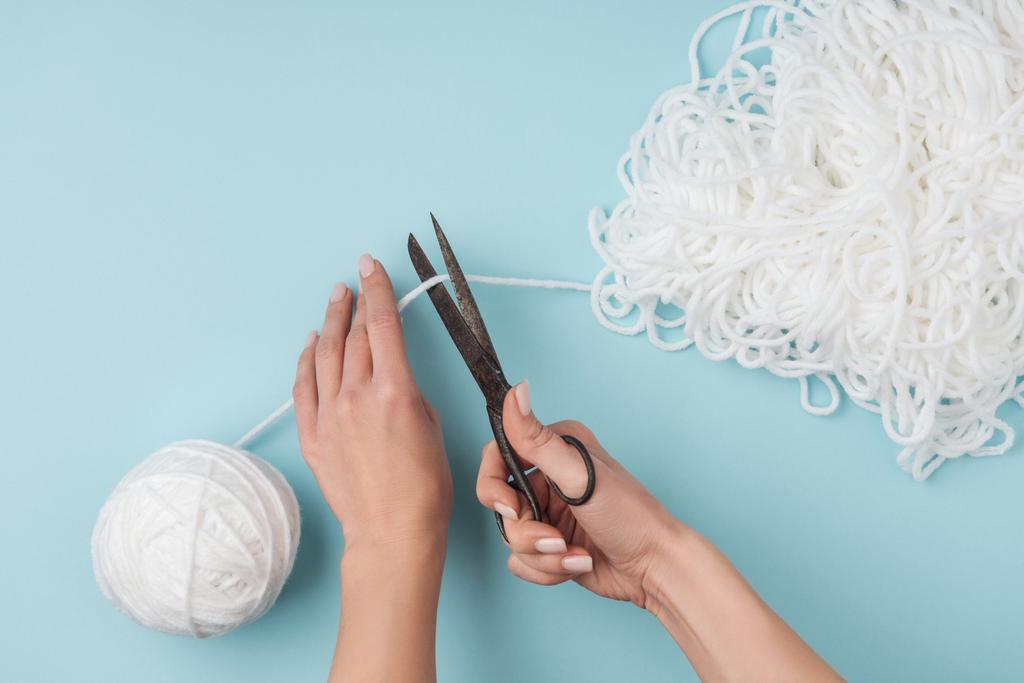 青い背景にハサミで糸を編む女性カット白のクロップ撮影 - 写真・画像