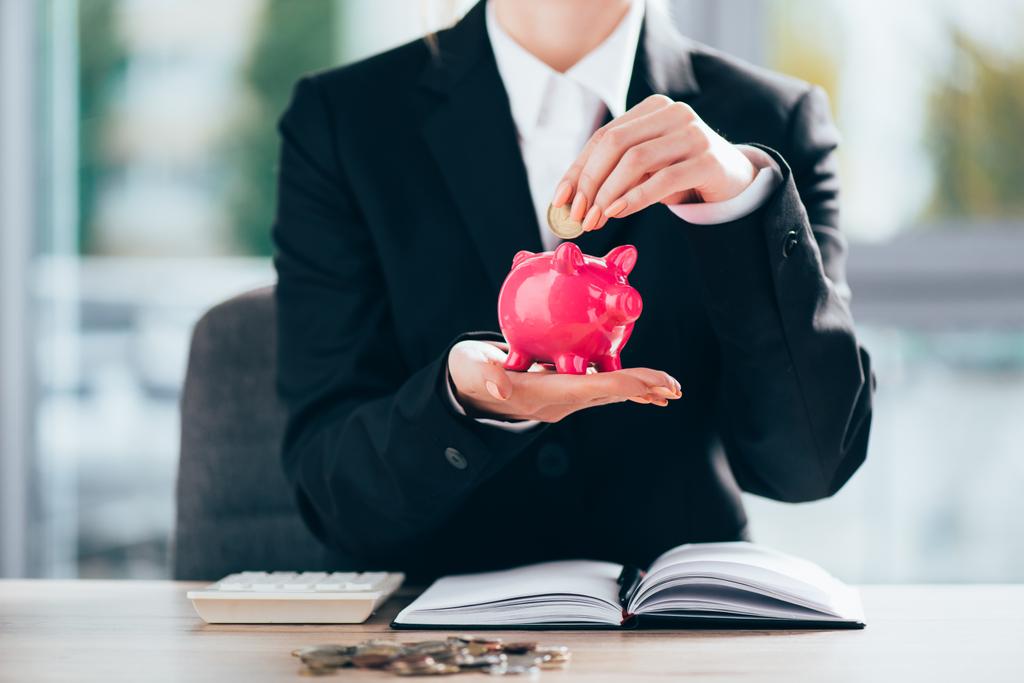 Schnappschuss von Geschäftsfrau, die Münze in rosa Sparschwein steckt  - Foto, Bild
