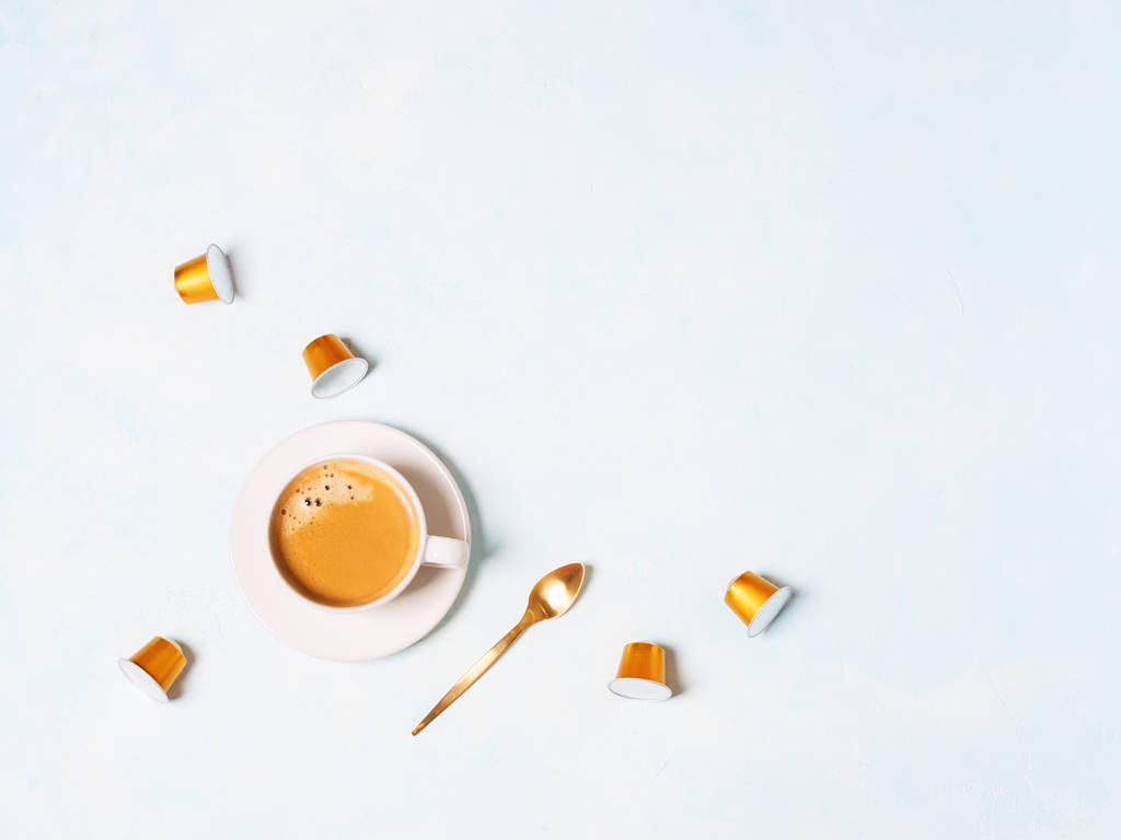 tazza di caffè espresso con capsule e cucchiaio d'oro su sfondo blu pastello
 - Foto, immagini