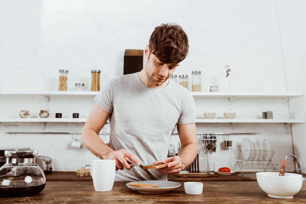 hombre guapo esparciendo tostadas por mermelada en la cocina en casa
 - Foto, Imagen