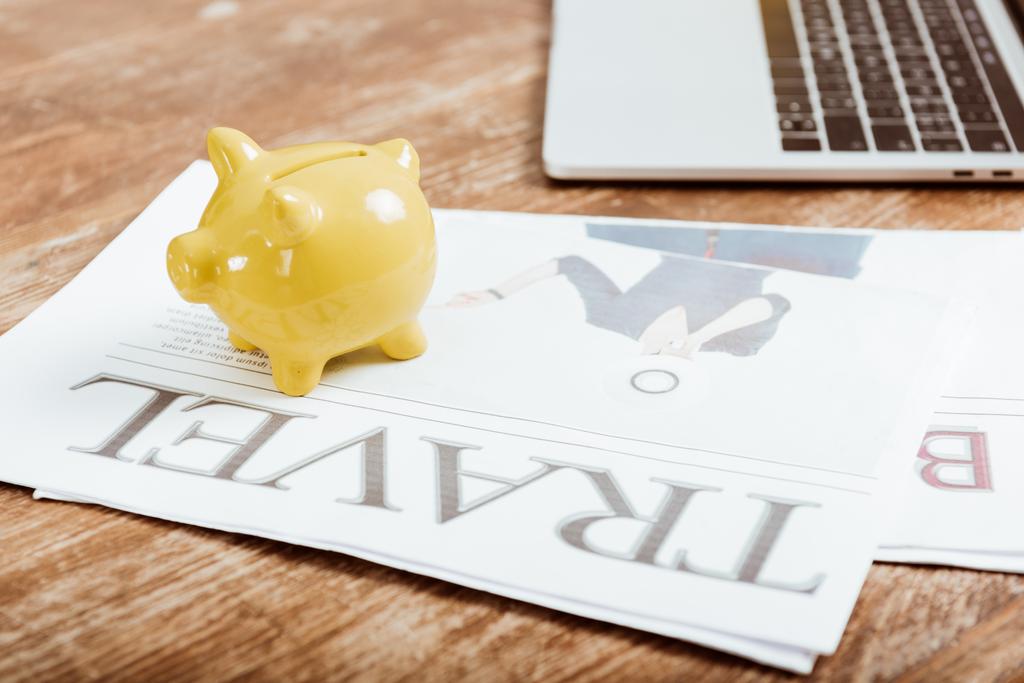 close up view of piggy bank on travel newspaper at table with laptop - Photo, Image