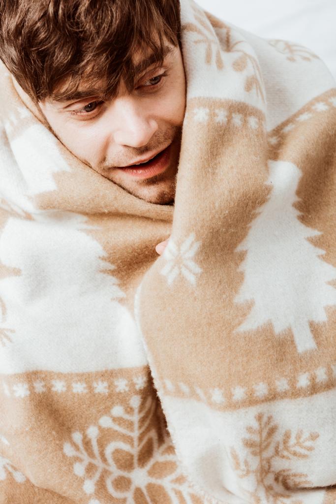 portrait of happy man wrapped in blanket sitting on bed at home - Photo, Image
