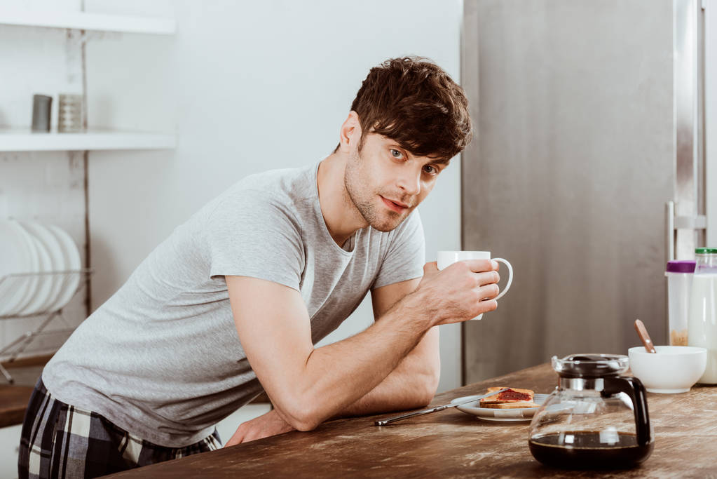 человек пьет кофе за столом с тостами и кофейник на кухне дома
 - Фото, изображение