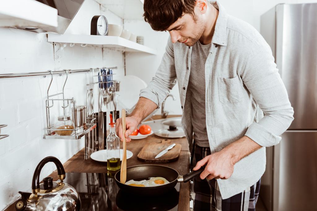 handsome young man making eggs on breakfast in kitchen at home - Photo, Image