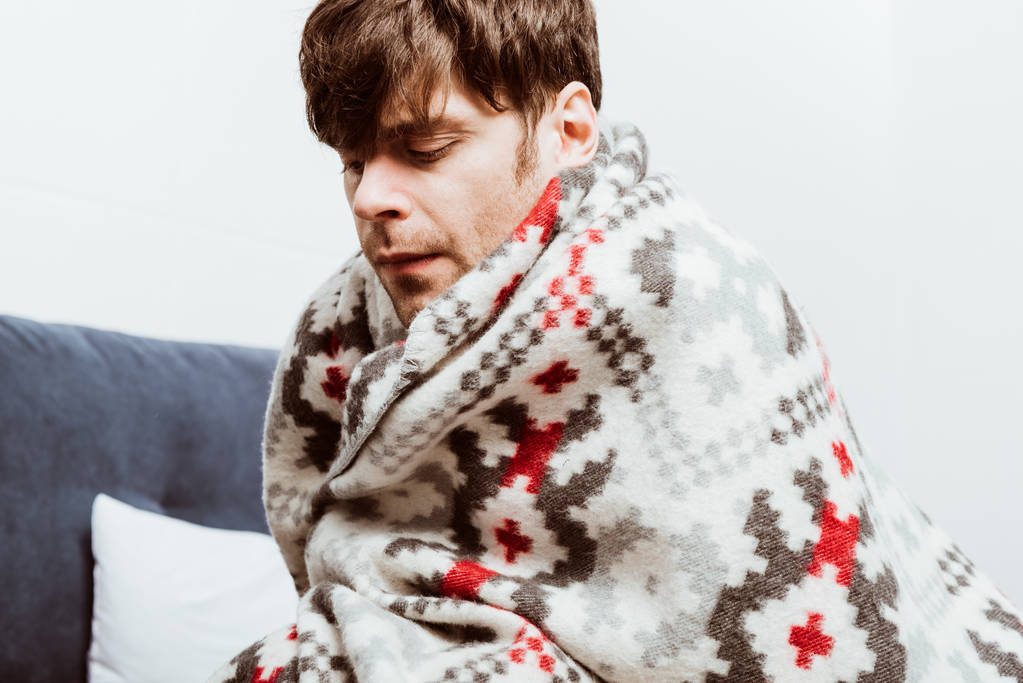 hasta genç adam yatakta evde oturan battaniyeye sarılmış - Fotoğraf, Görsel
