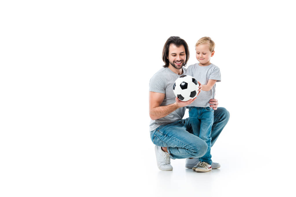 Daddy and his little child hugging each other and looking at soccer ball isolated on white - Photo, Image