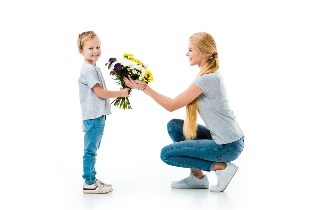 Hermosa madre con lindo hijo sosteniendo flores aisladas en blanco
 - Foto, imagen