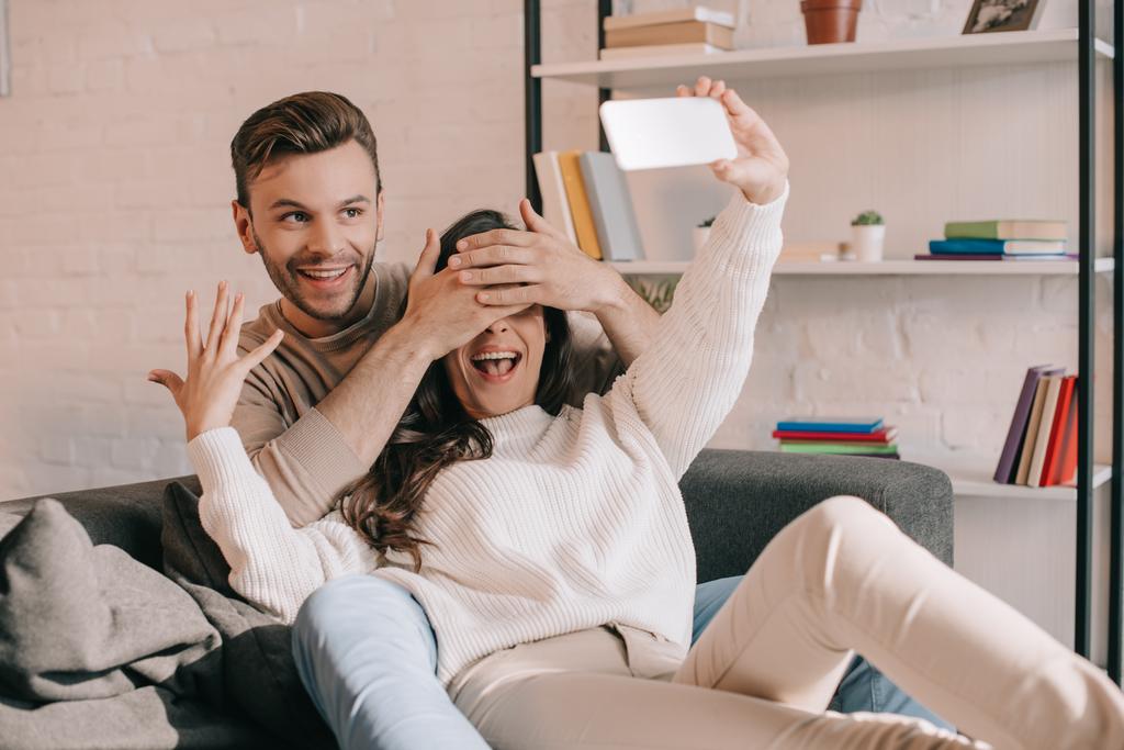 happy young couple taking selfie with smartphone on couch at home - Photo, Image