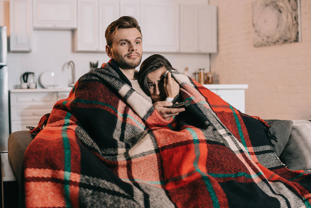 jovem casal relaxante no sofá e assistindo tv juntos enquanto cobre com xadrez
 - Foto, Imagem
