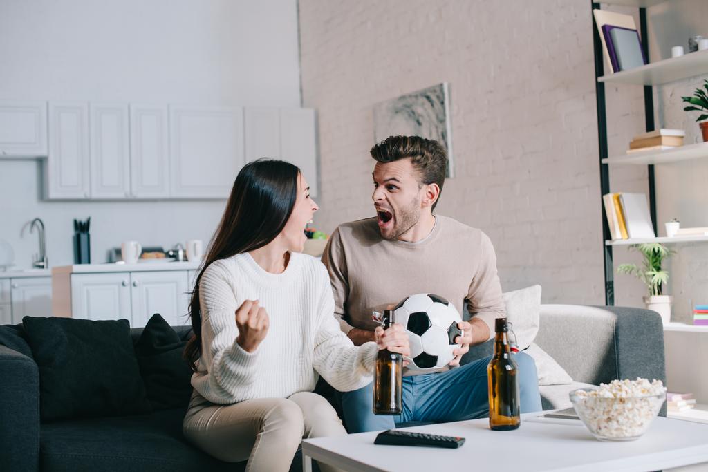 expressive young couple watching football game at home and cheering - Photo, Image
