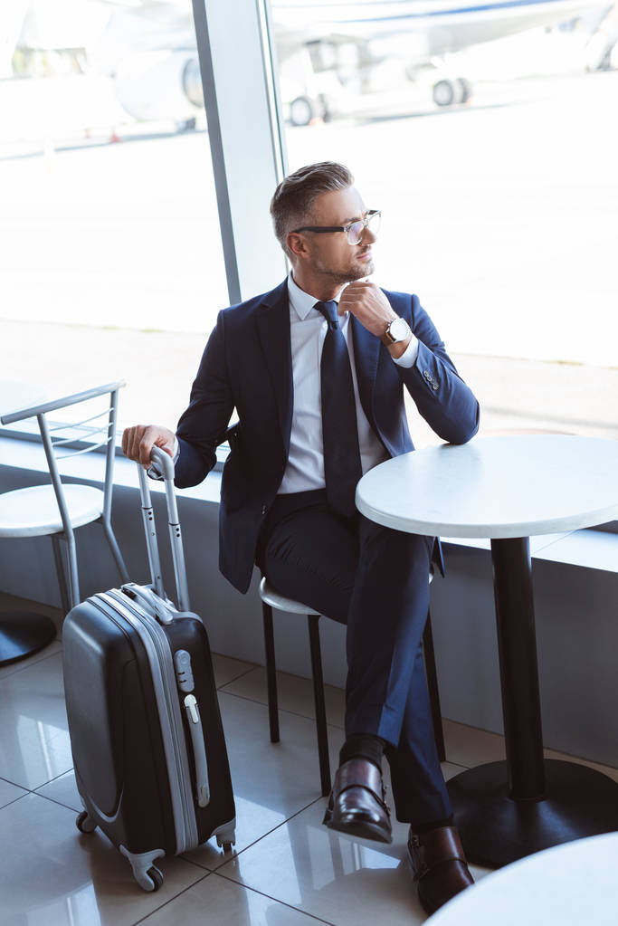 hombre de negocios adulto con bolsa de viaje sentado en la mesa en el aeropuerto
 - Foto, Imagen