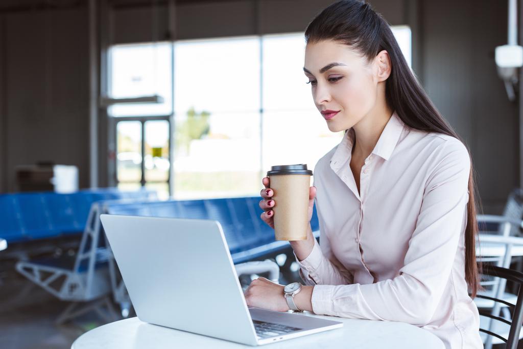 joven mujer de negocios con café para ir usando el ordenador portátil en el aeropuerto
 - Foto, imagen