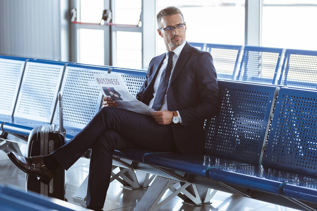 дорослий бізнесмен в окулярах сидить у від'їзді в аеропорту і читає газету
 - Фото, зображення