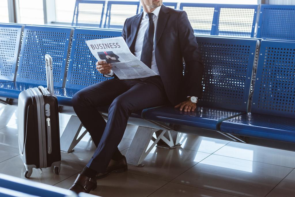 close up of adult businessman sitting at departure lounge at airport and reading newspaper - Photo, Image
