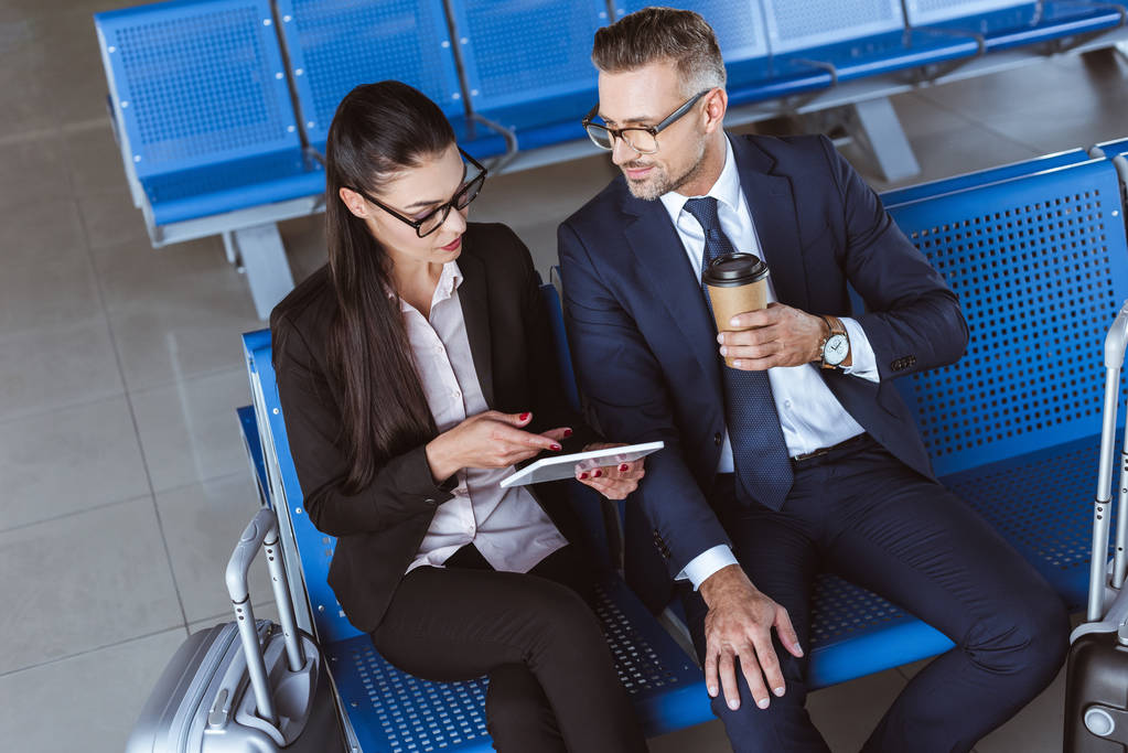 Erwachsener Geschäftsmann trinkt Kaffee, während Geschäftsfrau digitales Tablet in der Abflughalle am Flughafen benutzt  - Foto, Bild
