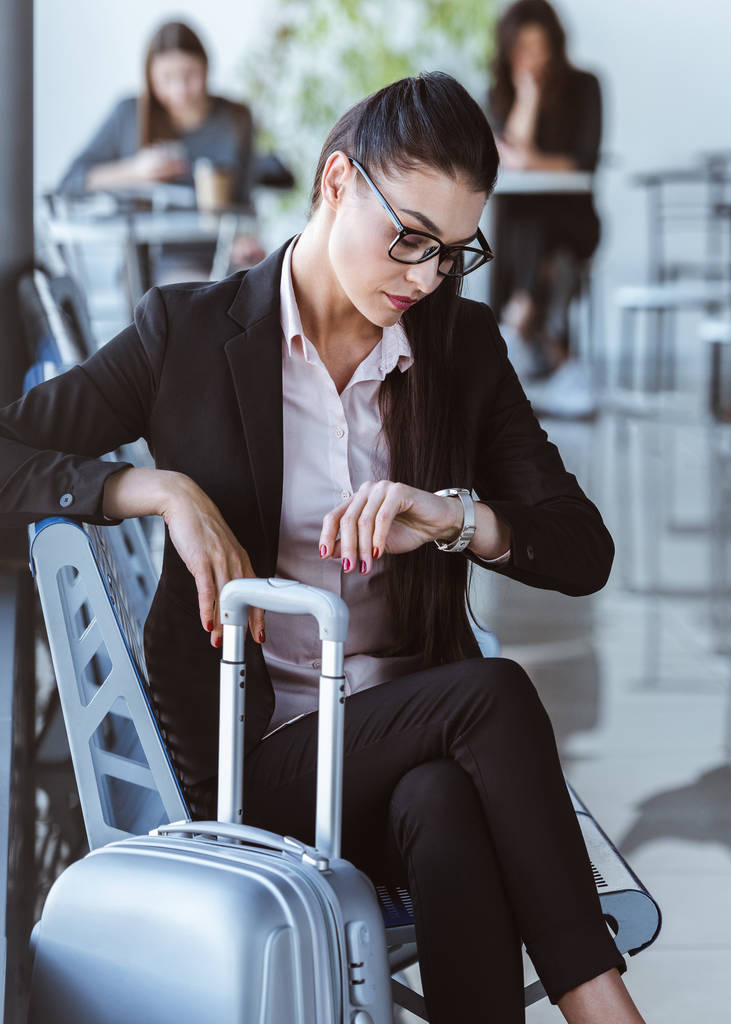 Взрослая деловая женщина смотрит на часы и ждет отъезда в аэропорту
 - Фото, изображение