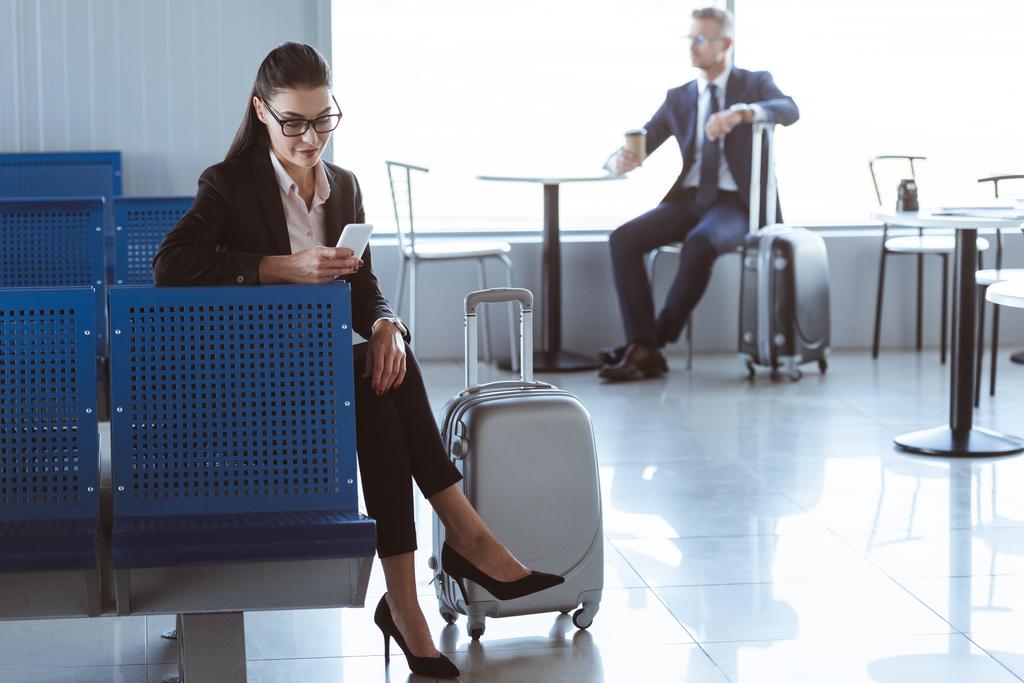 jonge zakenvrouw met smartphone terwijl zakenman zitten met koffie te gaan in de luchthaven - Foto, afbeelding