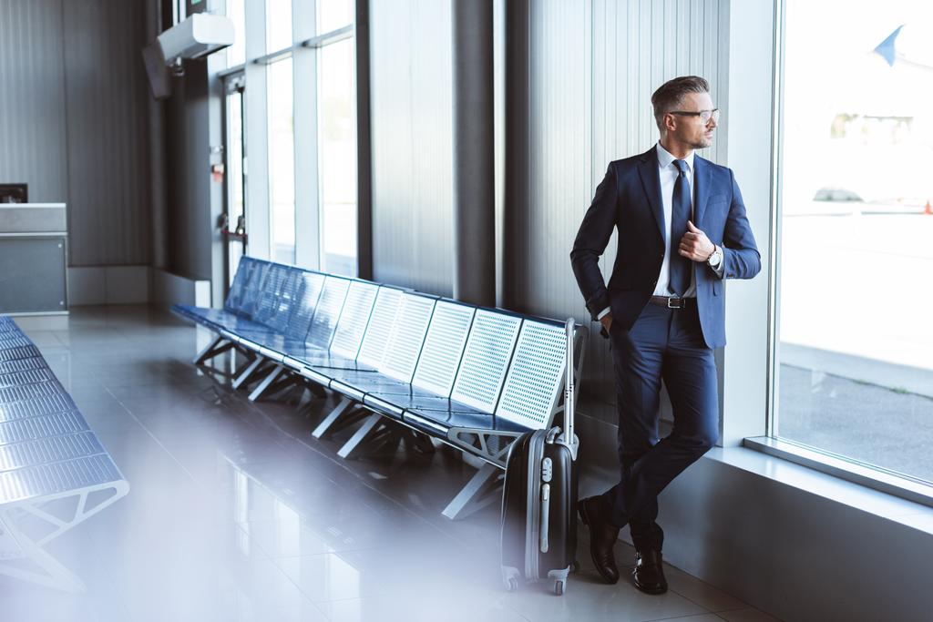 handsome businessman standing at departure lounge and looking at window in airport - Photo, Image
