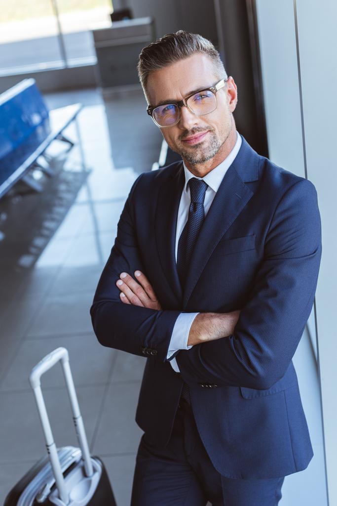 zakenman in glazen met armen gekruist staande in de luchthaven vertreklounge - Foto, afbeelding