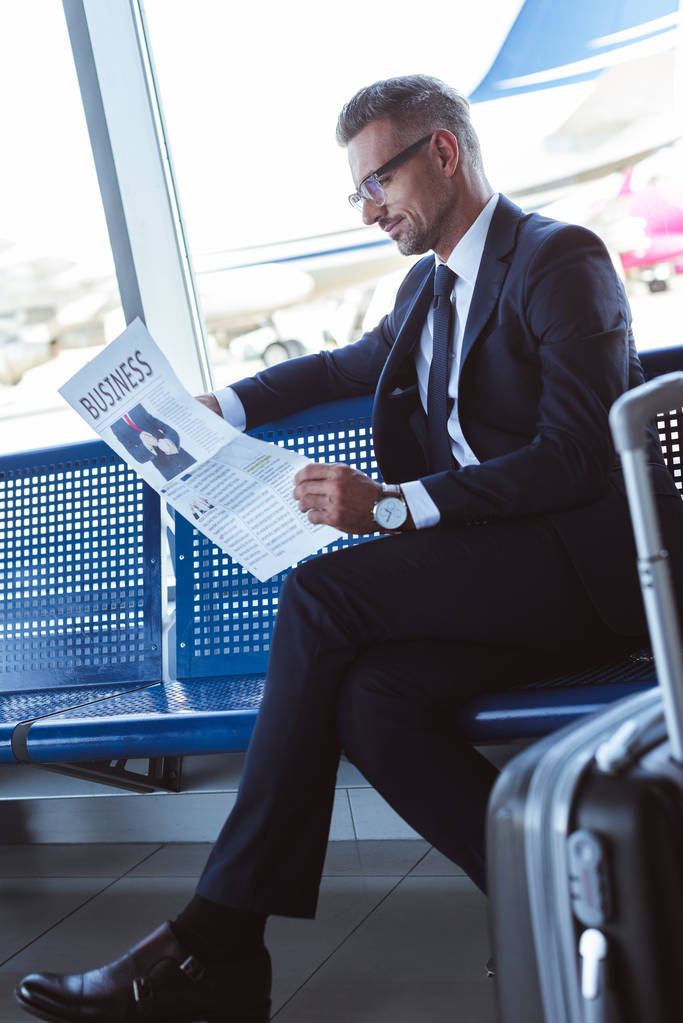handsome businessman sitting near window at departure lounge and reading newspaper - Photo, Image