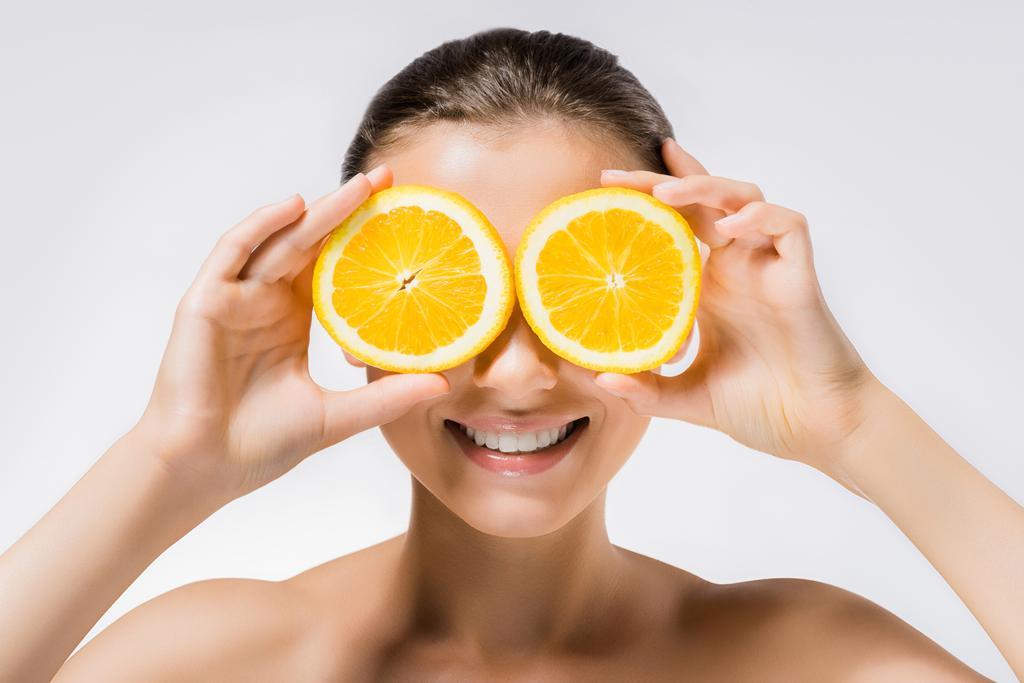 νεαρή γυναίκα χαμογελαστή με φέτες πορτοκαλιού για τα μάτια - Φωτογραφία, εικόνα
