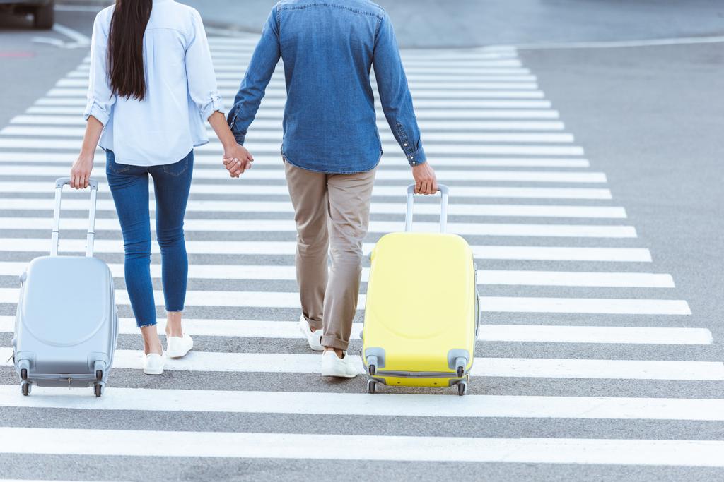Um casal de turistas atravessando pedestres, de mãos dadas e puxando sua bagagem
 - Foto, Imagem