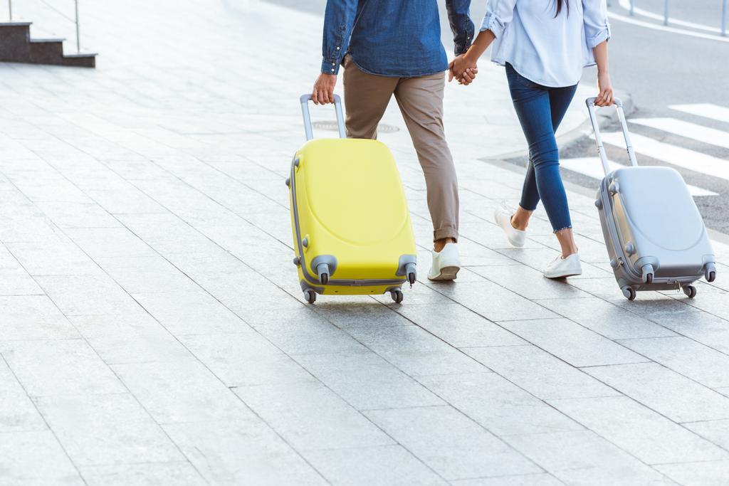 Gehakt zicht op een paar toeristen die elkaars hand vasthouden en hun bagage trekken - Foto, afbeelding