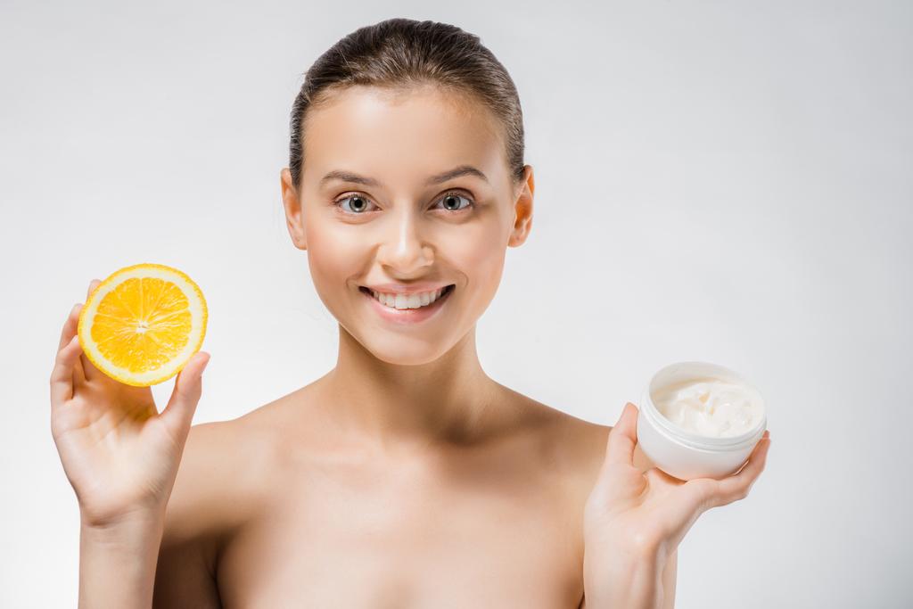молода красива жінка тримає білий крем для тіла і апельсиновий шматочок
 - Фото, зображення