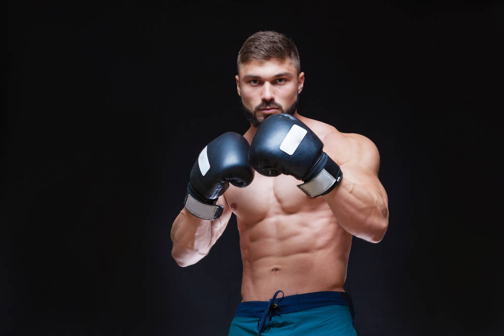 Boxeador musculoso fuerte con guantes de boxeo negros. Aislado sobre fondo negro
. - Foto, Imagen
