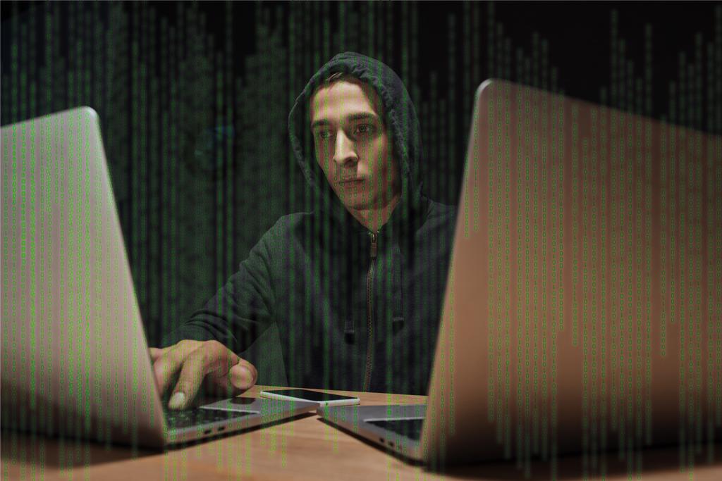 портрет хакера в черной толстовке с помощью ноутбуков на столе со смартфоном, концепция кибербезопасности
 - Фото, изображение