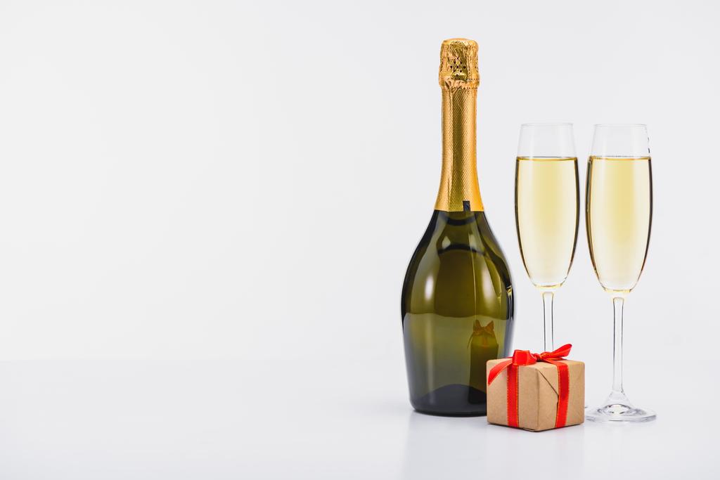 Nahaufnahme von Flasche und Glas Champagner mit eingewickeltem Geschenk auf weißem Hintergrund - Foto, Bild