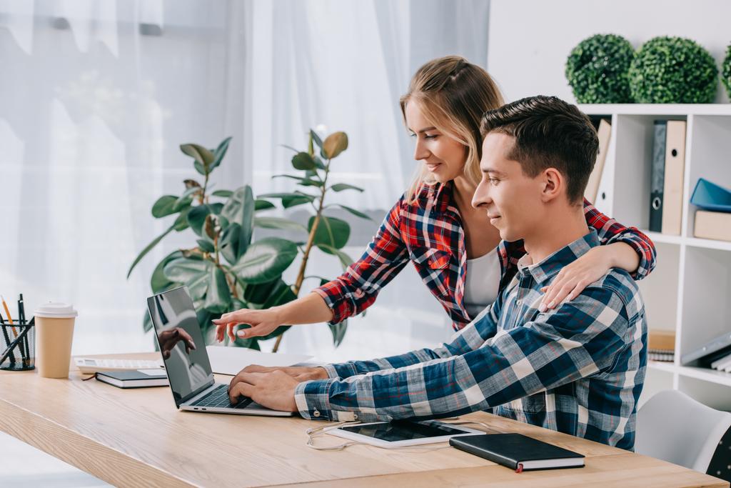 empresaria apuntando a la pantalla del ordenador portátil en blanco mientras participa en webinar junto con su colega en la oficina
 - Foto, imagen