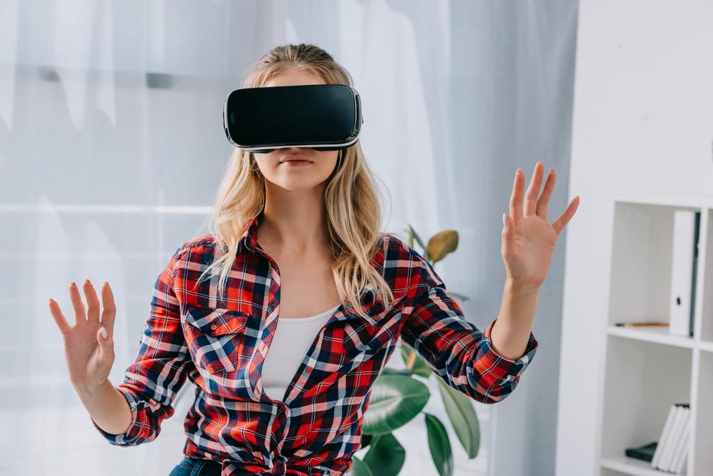 jovem mulher em realidade virtual fone de ouvido gesticulando no quarto
 - Foto, Imagem