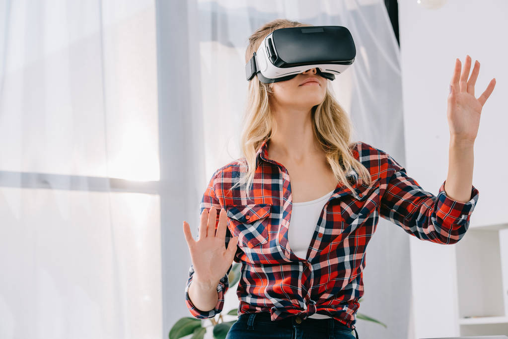 young woman in virtual reality headset gesturing in room - Photo, Image