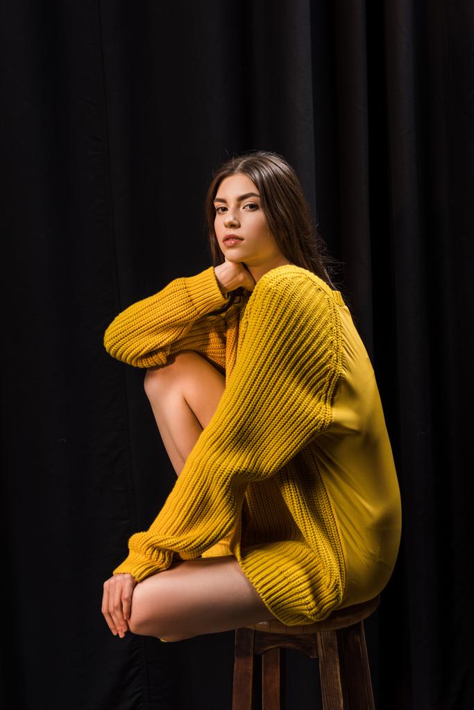 hermosa mujer en suéter de lana amarillo mirando a la cámara en el fondo negro
 - Foto, Imagen
