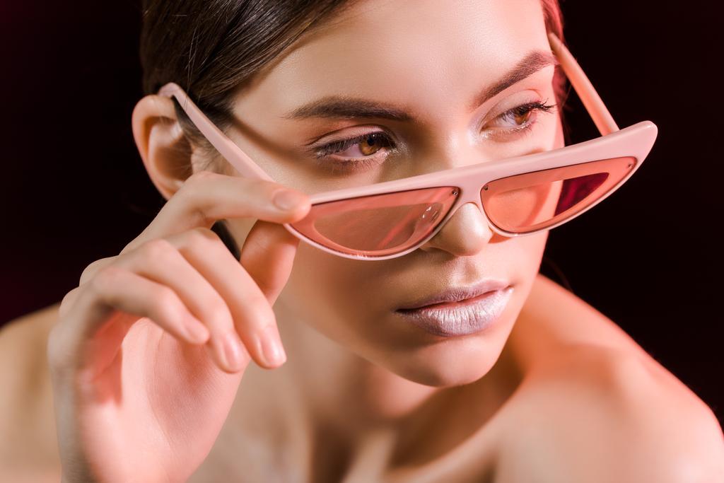 портрет красивой модели в модных очках, смотрящей вдаль изолированной на черном
 - Фото, изображение