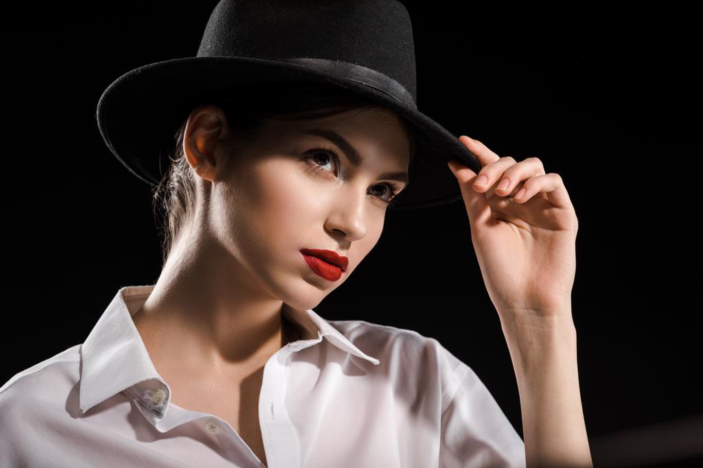 портрет красивої жінки в білій сорочці і чорний капелюх позує ізольовано на чорному
 - Фото, зображення