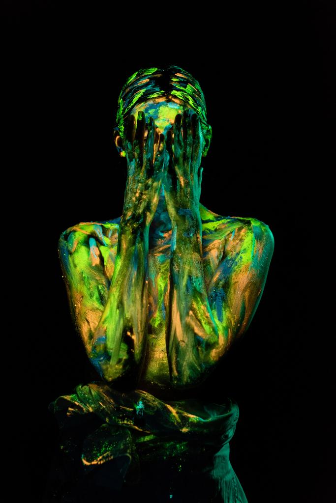 vista oscurecida de la mujer pintada con pinturas ultravioletas cubriendo la cara sobre fondo negro
 - Foto, imagen