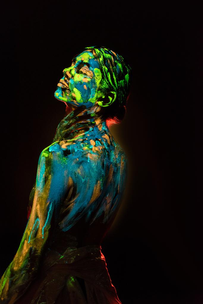 vista laterale della donna dipinta con colorate vernici a raggi ultravioletti su sfondo nero
 - Foto, immagini