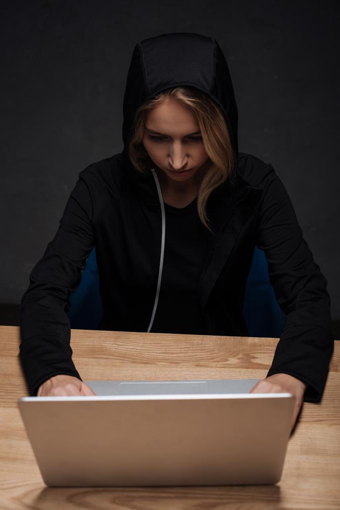 kadın hacker ahşap masa üstü dizüstü kullanarak siyah hoodie'odaklı - Fotoğraf, Görsel